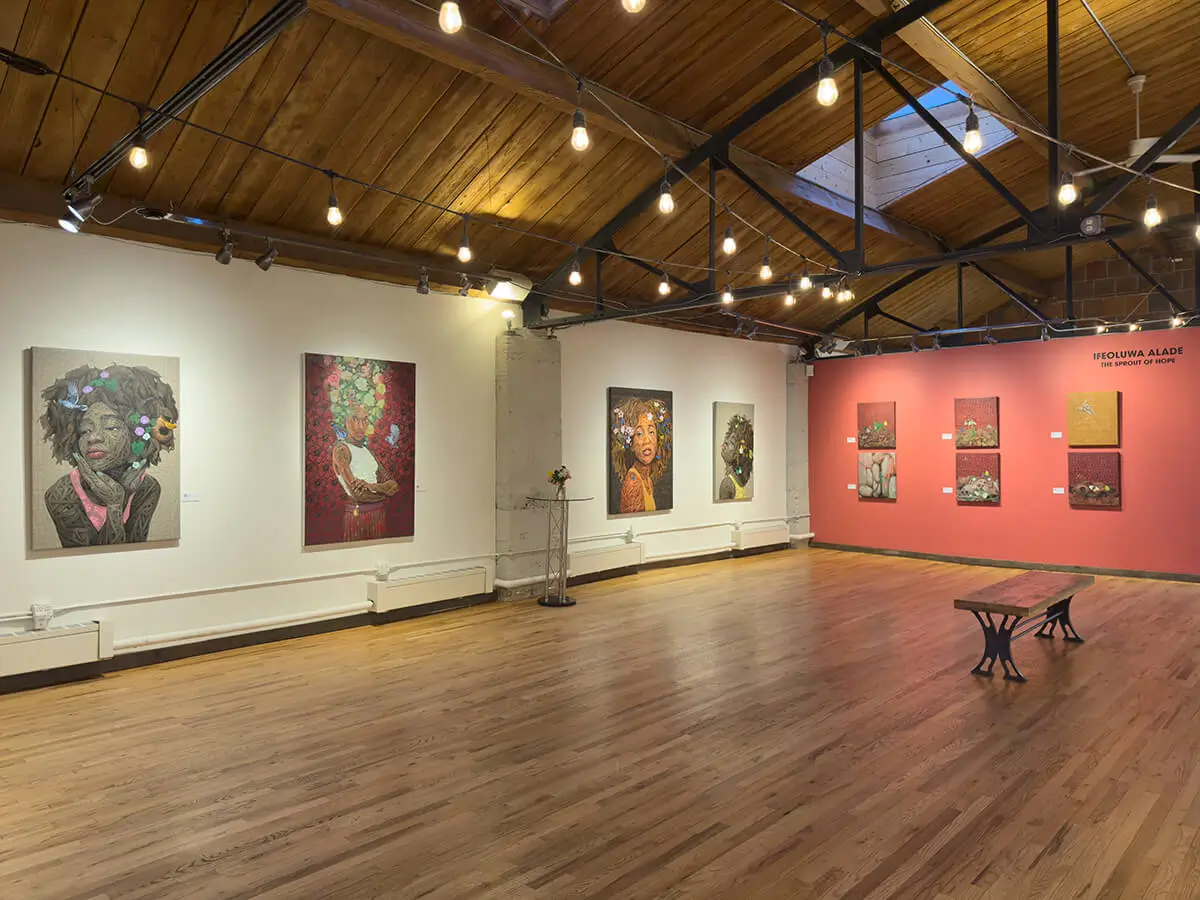 Expansive gallery installation of The Sprout of Hope by Ifeoluwa Alade. Portraits on the left wall include Still I Rise (2) in a red dress, Beulah with white blossoms, and Oasis with pink flowers and butterflies. A coral wall holds smaller nature-inspired paintings with skulls, butterflies, and greenery. String lights hang above a wood floor and bench.