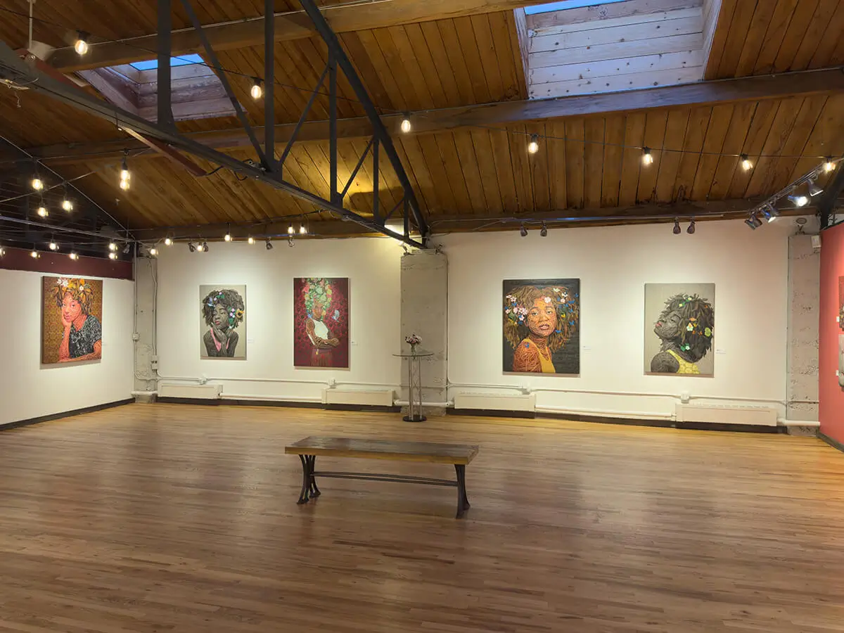 Installation shot featuring Ifeoluwa Alade’s Beulah, Still I Rise (2), and Oasis in conversation with her Light in the Darkness series on the coral wall. The central bench, wooden flooring, and delicate string lighting contribute to the warm, immersive setting of Abend Gallery.