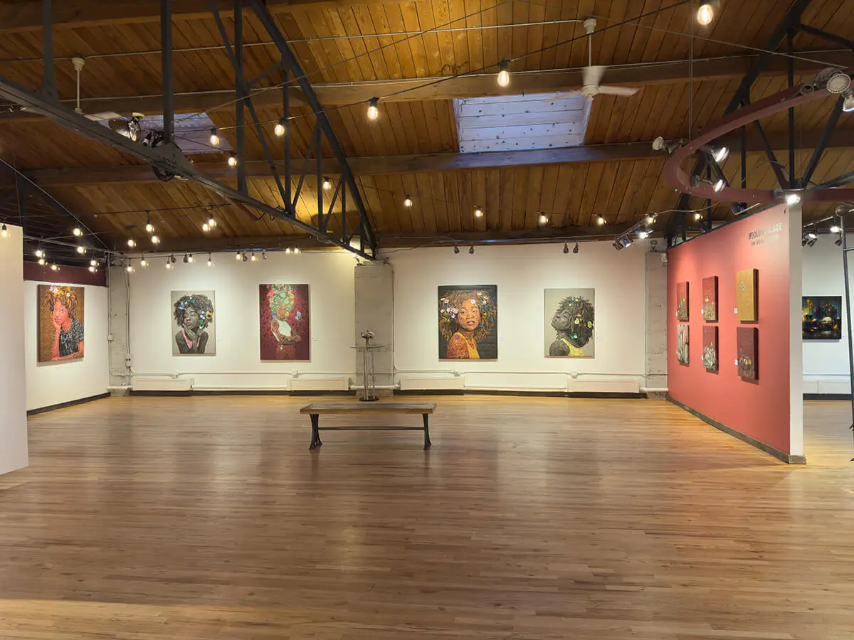Gallery-wide photo of Ifeoluwa Alade’s The Sprout of Hope at Abend Gallery, showing both figural and symbolic works. On the back wall: Beulah, Still I Rise (2), Oasis, and Still I Rise (1). To the right, The Mustard Seed and Light in the Darkness I–IV hang against a coral backdrop. The room’s string lights and hardwood floors create a calm, reflective viewing experience.